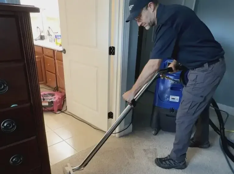 A technician running a portable extractor over soaked hallway carpet